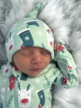 Sleeping baby in festive green outfit with holiday patterns, resting on a soft, fluffy surface.