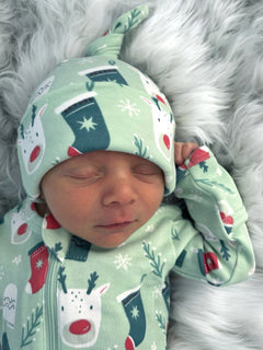Sleeping baby in festive green outfit with holiday patterns, resting on a soft, fluffy surface.