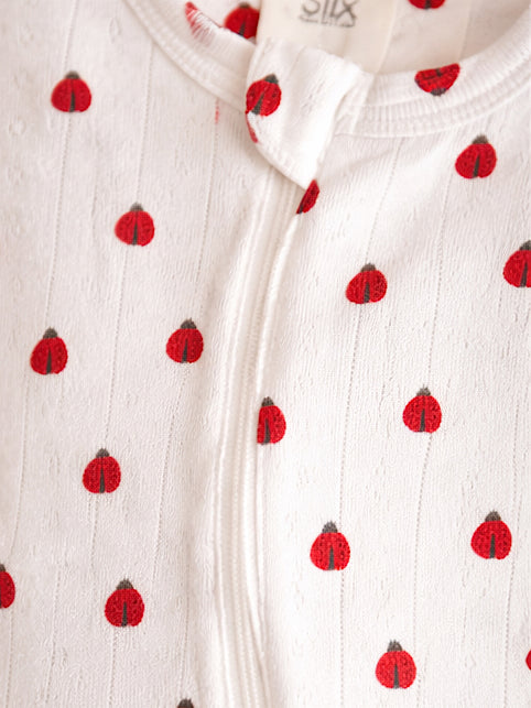 White fabric with small red ladybug patterns, featuring a zipper closure at the front.