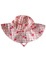 Children's sun hat with cherry print on a pink gingham background, featuring a wide brim and adjustable straps.