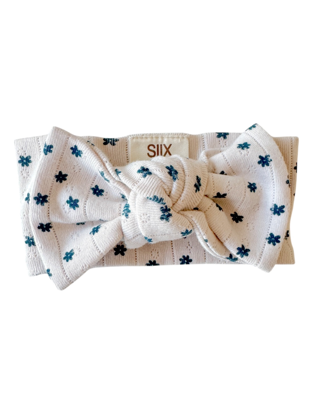 White headband with a large bow and dotted floral pattern in blue, labeled with brand name 