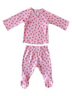 Pink children's pajama set features long sleeves and patterned with small red hearts. 