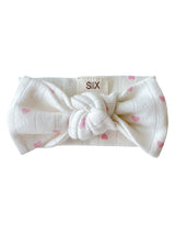 White headband with pink heart pattern and a knot at the front, labeled "SIIX." Ideal for casual or sporty styles.