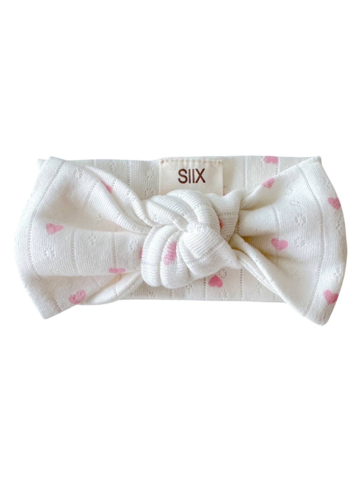 White headband with pink heart pattern and a knot at the front, labeled 