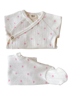 White baby outfit featuring pink heart patterns, including a top, pants, and hat.
