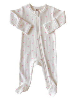 White baby onesie with pink heart patterns and a front zipper, featuring long sleeves and footed legs.