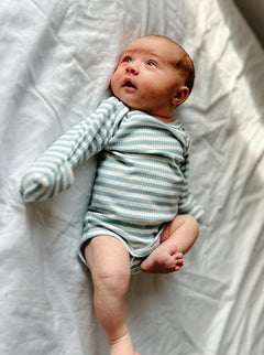 Infant in a striped onesie lying on a white surface, looking up with wide eyes.