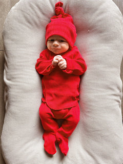 Baby in a red outfit and hat, smiling while lying on a textured cream-colored surface.