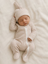 Newborn baby in a striped onesie and matching hat, peacefully sleeping on a soft, light-colored blanket.