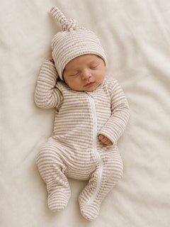 Newborn baby in a striped onesie and matching hat, peacefully sleeping on a soft, light-colored blanket.