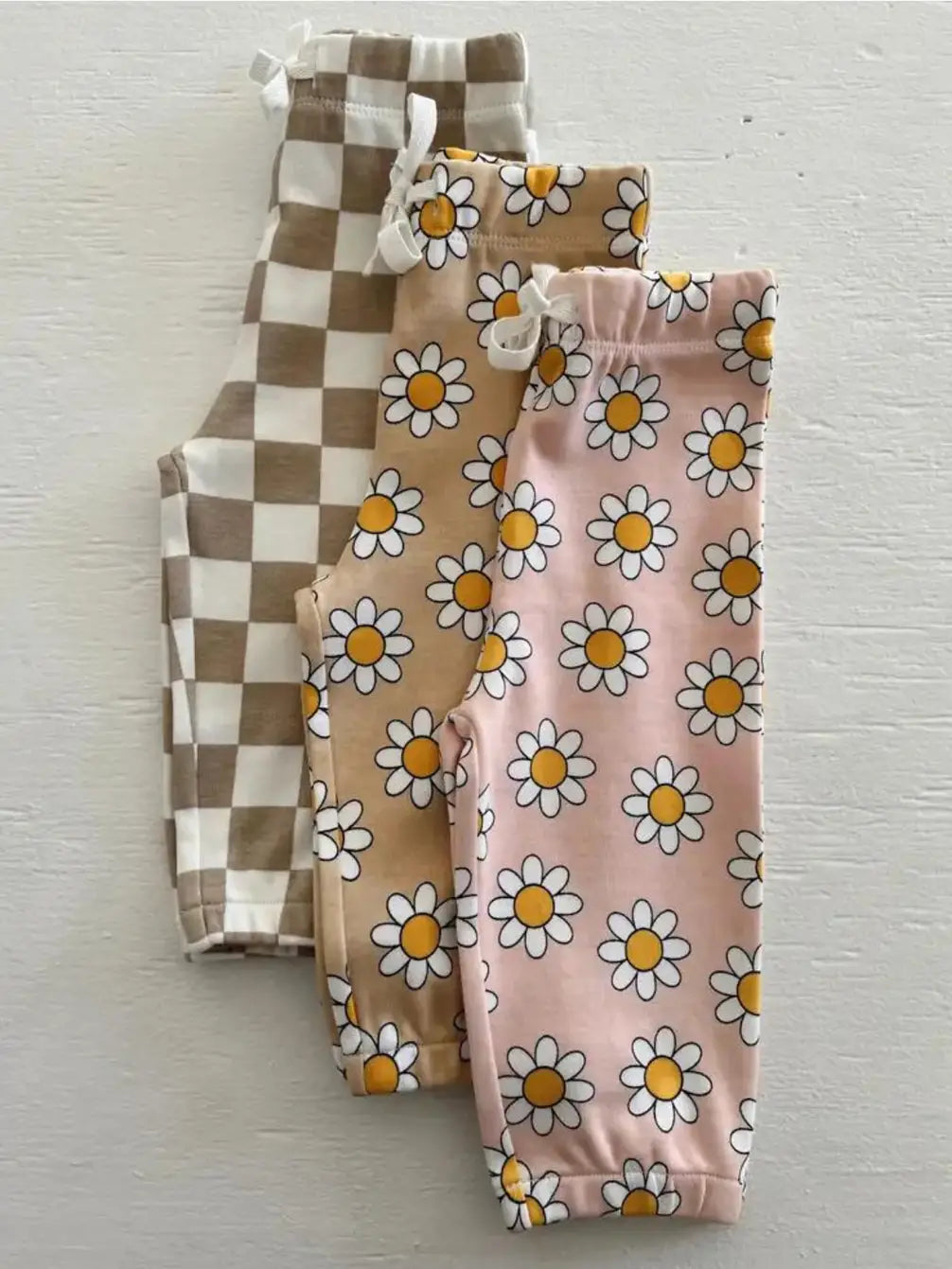 Three pairs of children's leggings featuring floral and checkered patterns in soft hues.