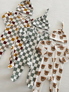 Two baby onesies in plaid patterns and one with bear prints, paired with matching knotted hats.