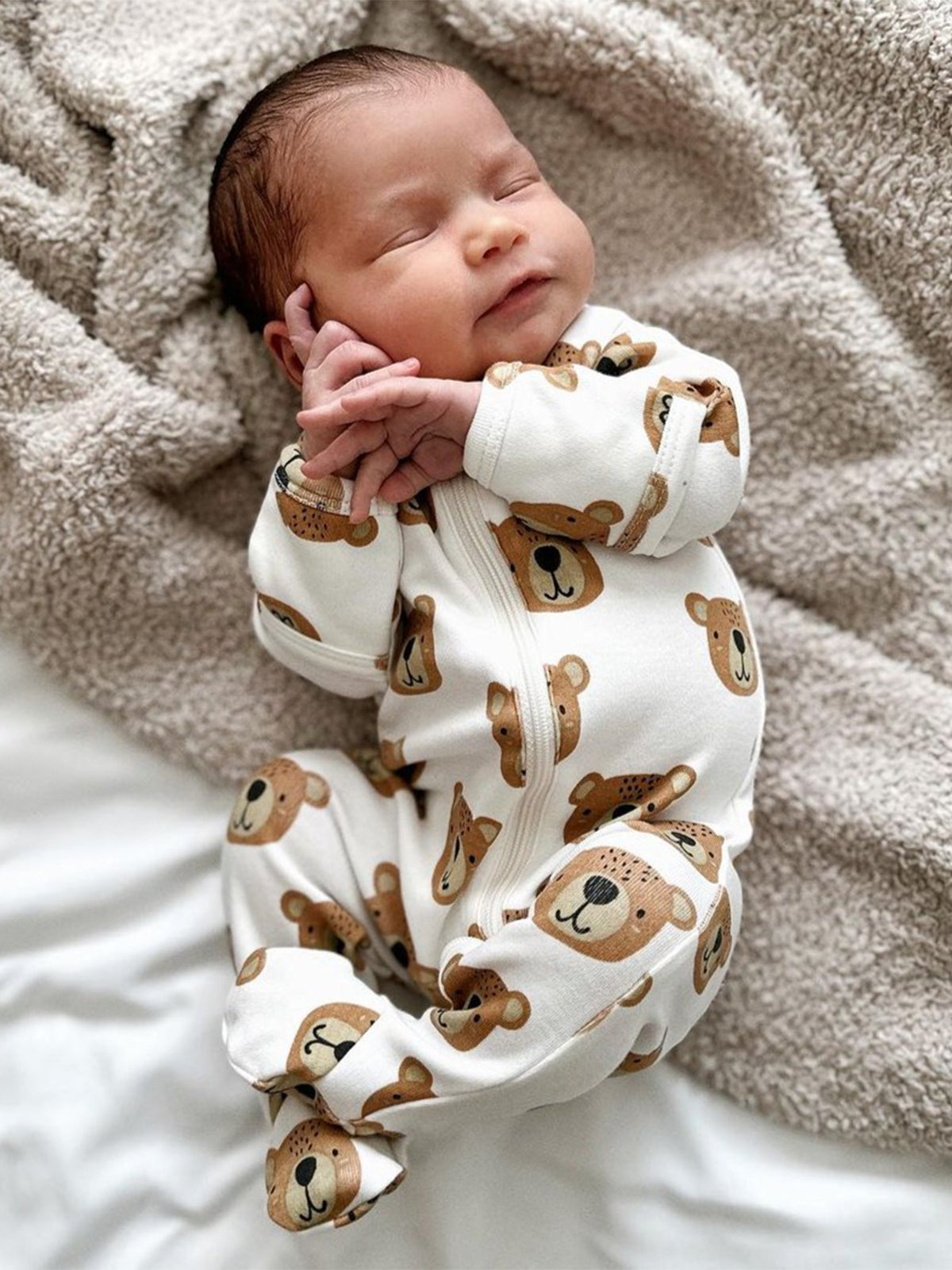 Baby peacefully sleeping in cozy bear-patterned outfit, lying on soft blanket.