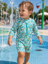 Smiling child in a colorful swimsuit playing in a splash pad, surrounded by water sprays on a sunny day.