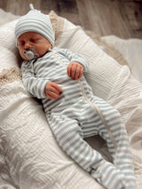 Infant in blue-striped outfit and hat, sleeping peacefully on a textured white blanket.