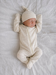 Newborn baby peacefully sleeping on a soft blanket, wearing a cream-colored outfit and a matching hat.