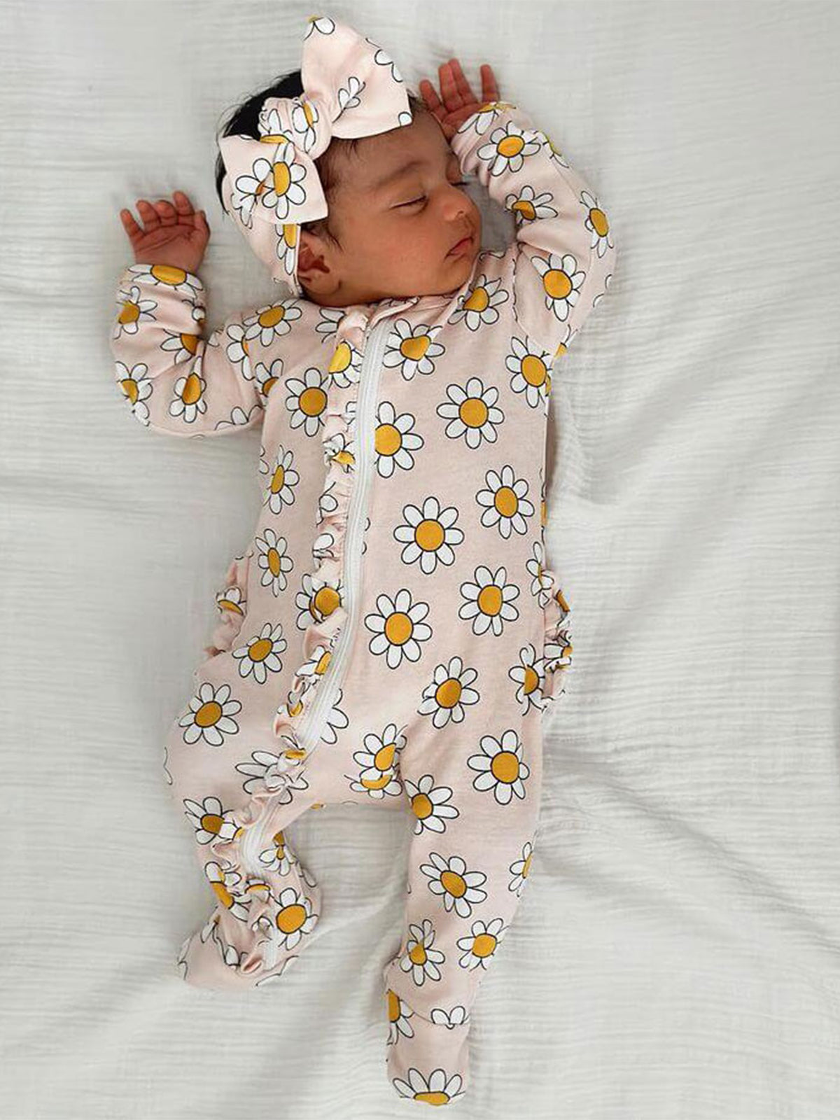 Baby sleeping in a floral onesie and matching headband on a white background.