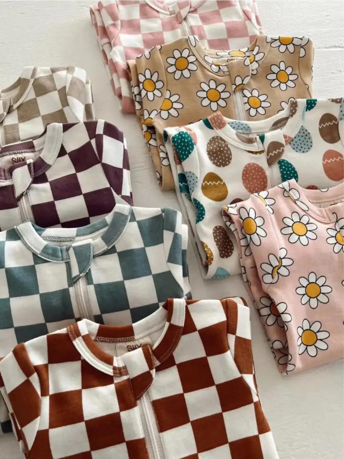 Assorted baby bodysuits in pastel colors, featuring floral and checked patterns, neatly folded on a flat surface.