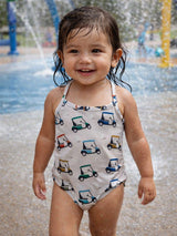 Smiling toddler in a patterned swimsuit standing in a splash pad, with water droplets around them.