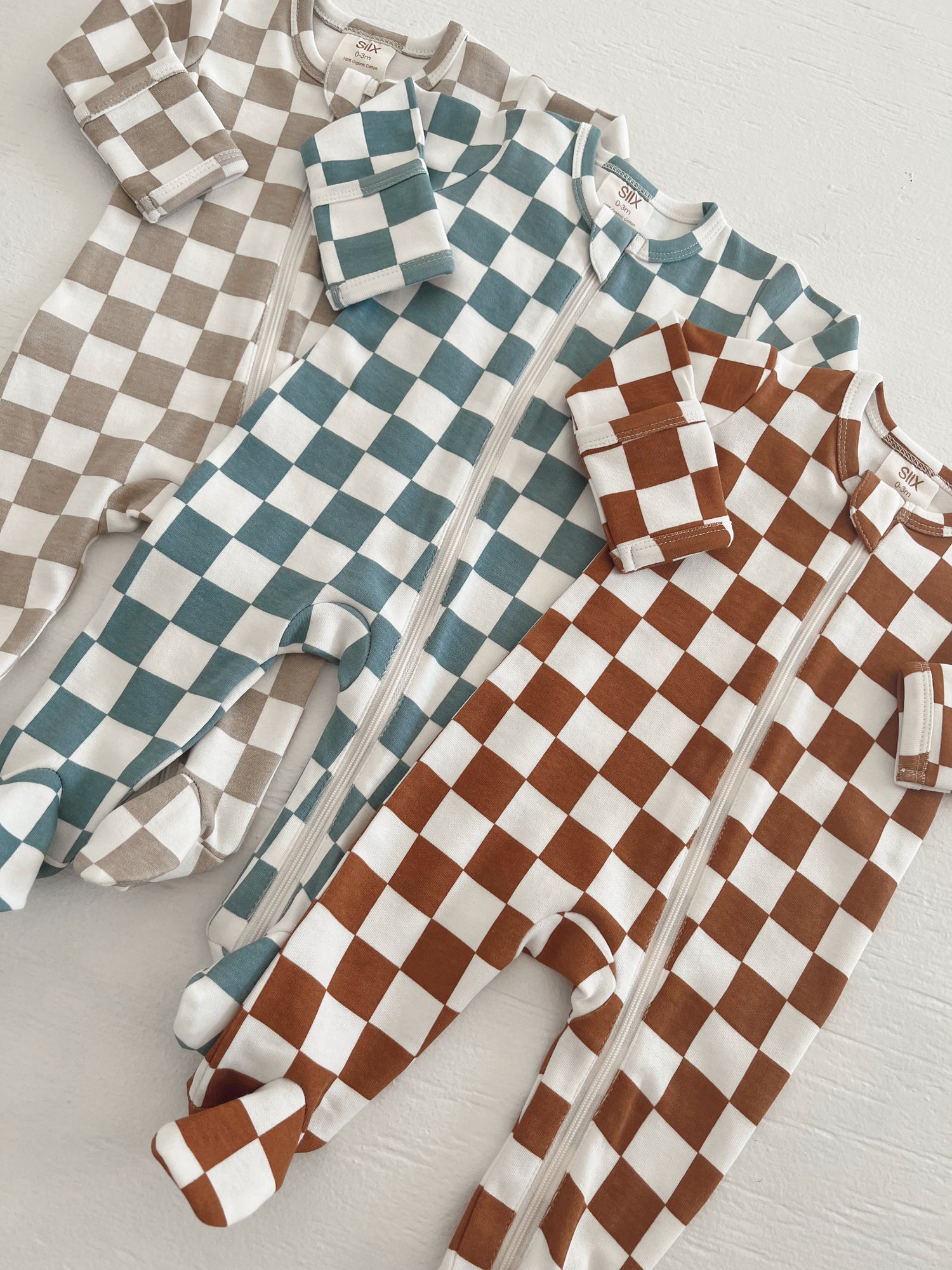 Three checkered baby onesies in brown, teal, and white, displayed on a light background.