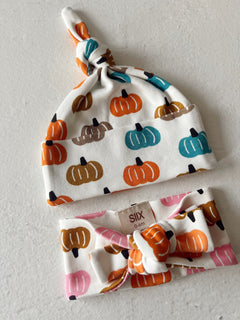 Two baby headbands: a knotted hat with colorful pumpkins and a pink stretchy headband with a bow, both for ages 0-6 months.