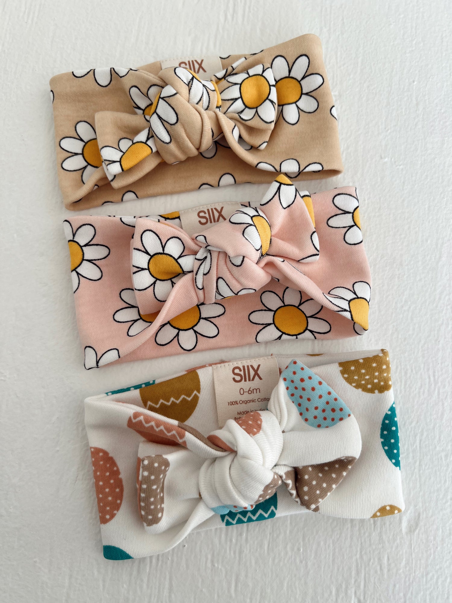 Three baby headbands: floral patterns in beige, pink, and white with colorful dots and shapes.