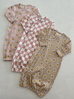 Three cute children's sleepers in pastel colors with floral and checkered patterns on a light background.