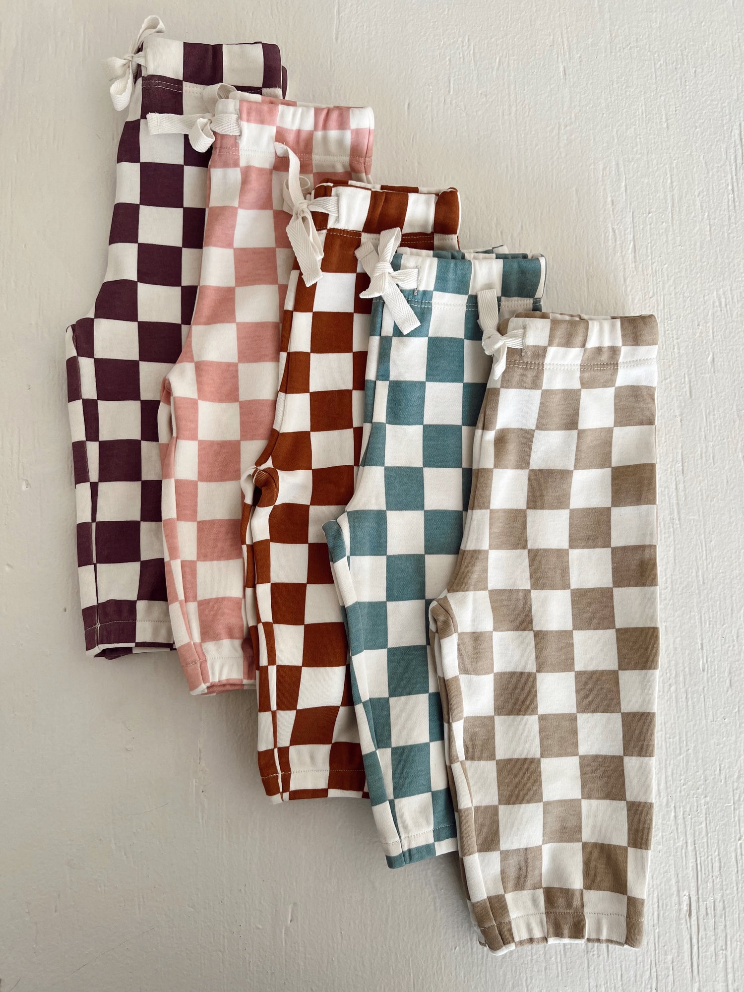 Colorful checkered pants in purple, pink, brown, teal, and beige arranged in a row on a light background.