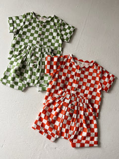 Two checkered outfits in green and orange hues, featuring short sleeves and button details.