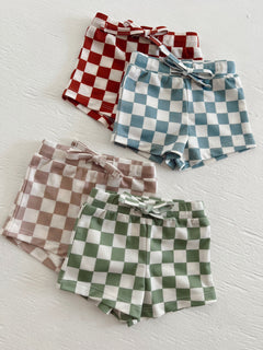 Four pairs of checked shorts in red, blue, green, and brown laid out on a white surface.