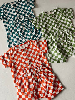 Four checkered outfits in teal, green, orange, and white, featuring buttons and elastic waistbands.