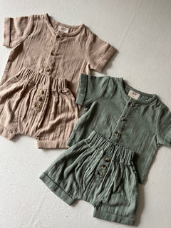 Two sets of infant romper outfits in beige and green with buttons, arranged on a neutral background.