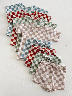 Assorted checkered kids' outfits in various colors, including red, green, and blue, laid out on a white surface.