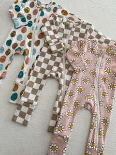 Three infant onesies: one with colorful eggs, one in a brown check pattern, and one with yellow daisies on pink.