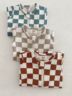 Three checkered infant onesies in teal, beige, and rust stacked against a white background.