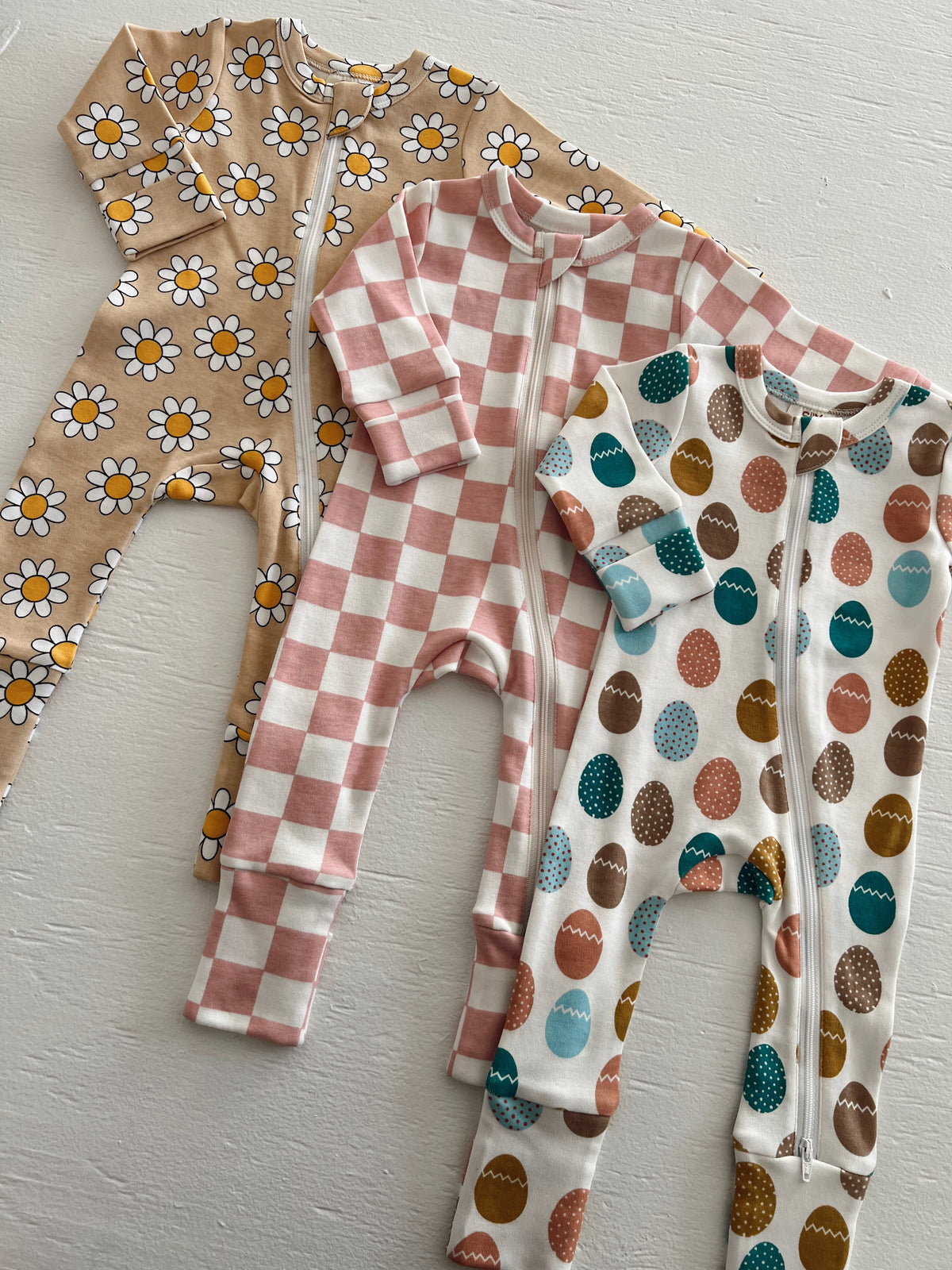 Three children’s pajamas: floral, checkered, and egg-patterned designs displayed on a light surface.