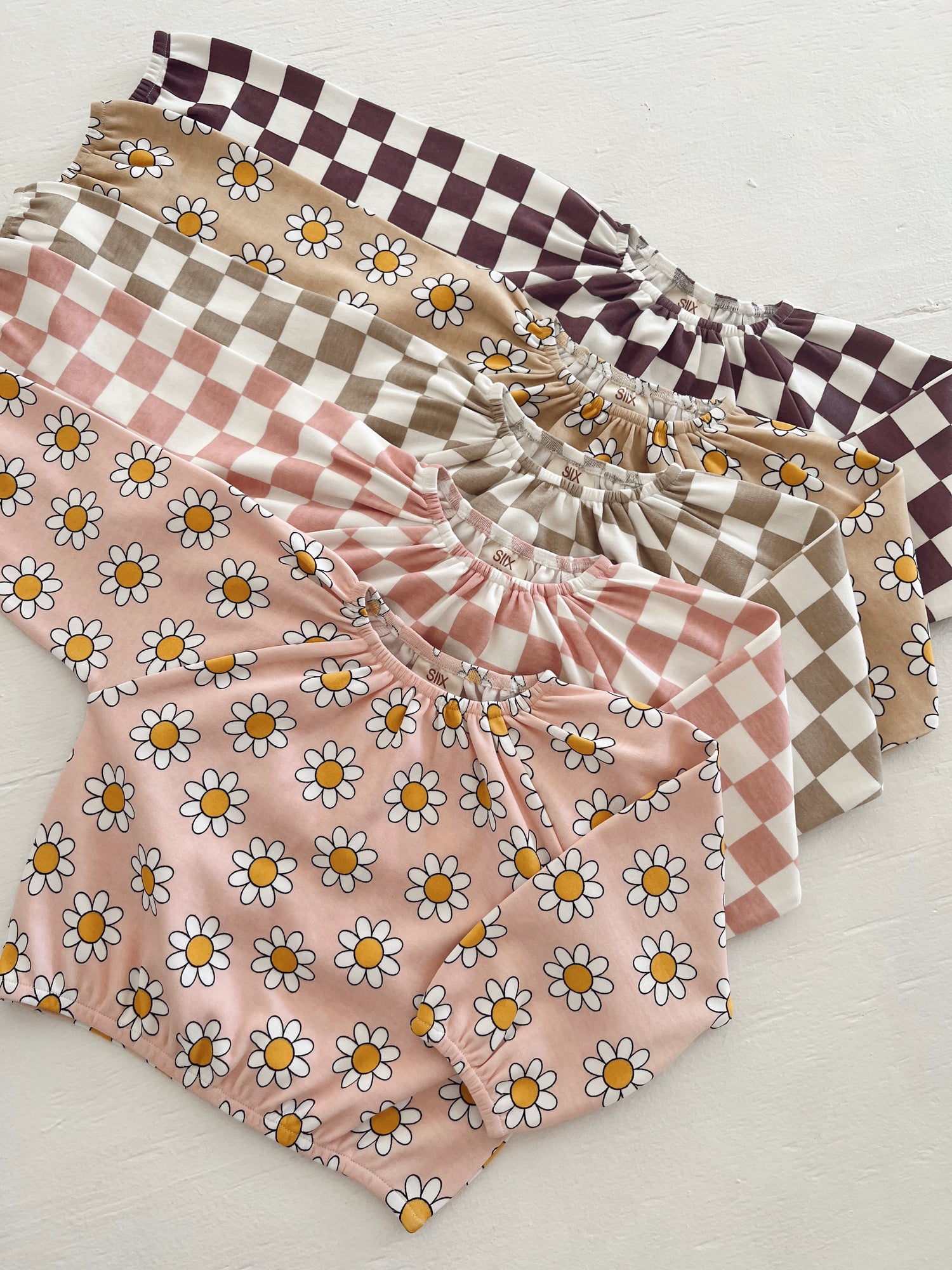 Colorful children's tops with floral and checkered patterns stacked on a light background.