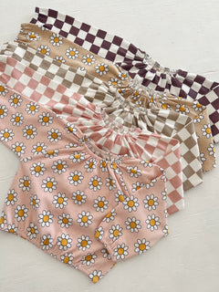 Colorful children's tops with floral and checkered patterns stacked on a light background.