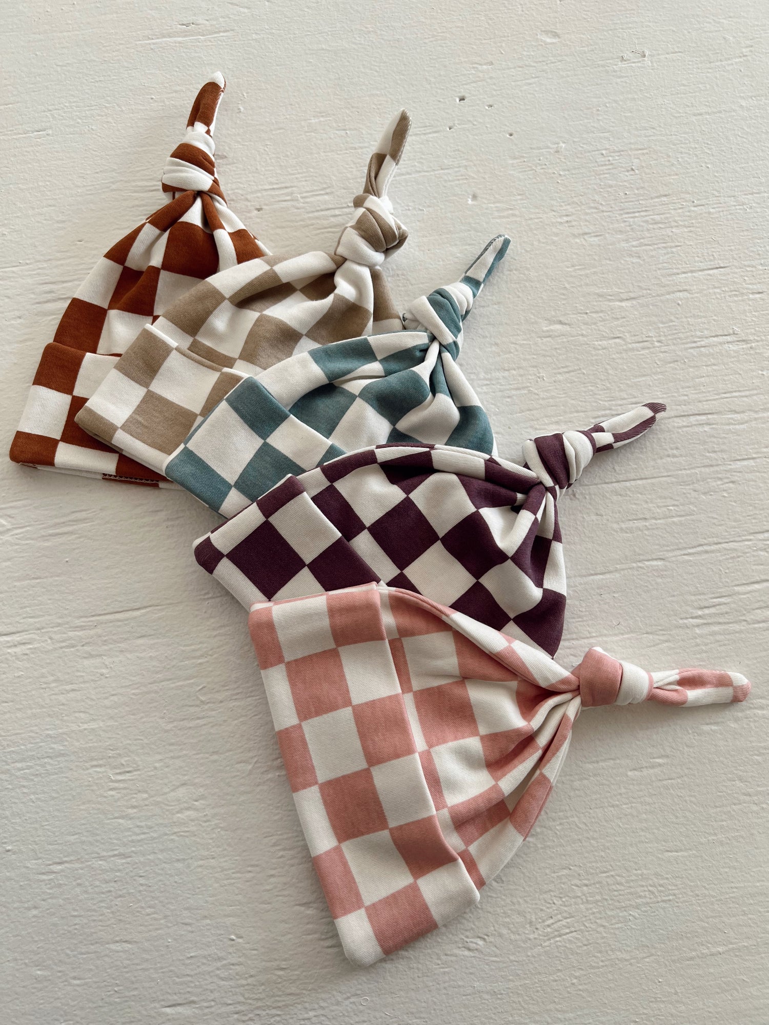 Four checkered toddler hats in various colors: rust, teal, burgundy, and pink, displayed on a light surface.