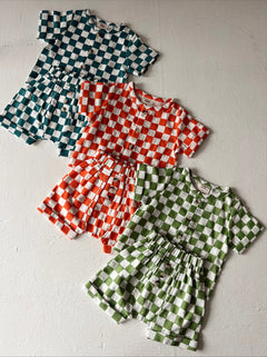 Four checkered baby outfits in green, orange, teal, and white laid on a light textured surface.