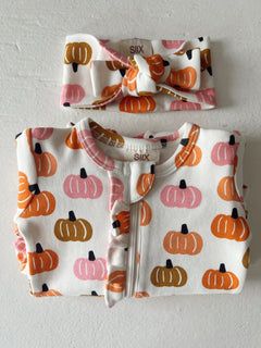 Baby outfit set with pumpkin prints, includes a zip onesie and matching headband. Ideal for fall fashion.