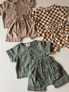 Children's clothing set featuring two short-sleeve shirts and matching shorts in neutral and checkered patterns.
