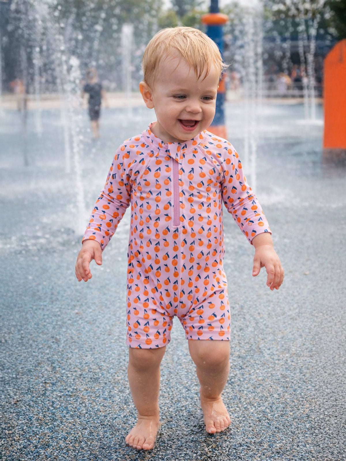 Child in playful water park, wearing a colorful swimsuit, smiling joyfully amidst splashing water.