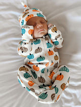  newborn sleeping in pumpkin-patterned outfit on a white blanket