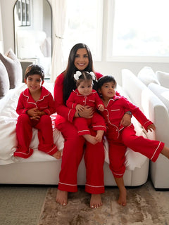 Mother and three children in matching red pajamas, sitting on a bed with bright natural light in the background.