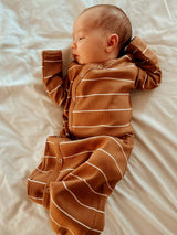 A peaceful baby wearing a brown striped onesie, lying on a light-colored blanket.