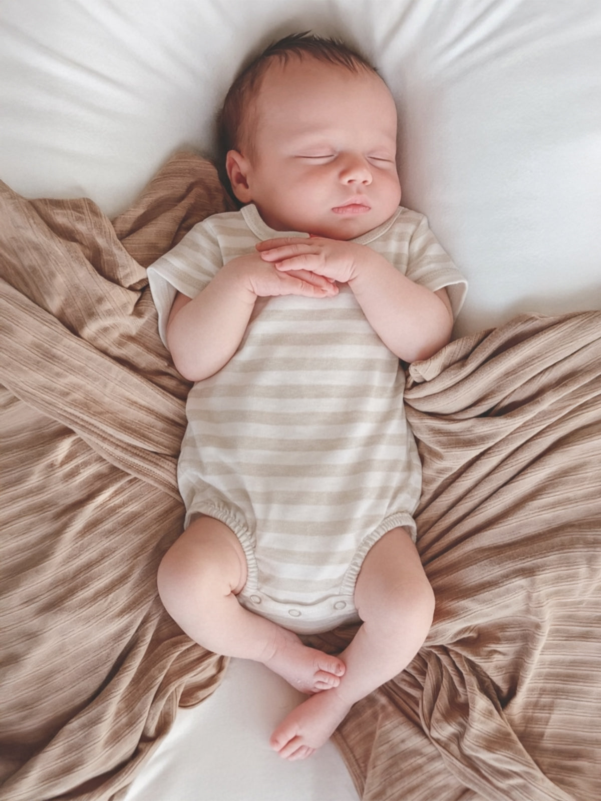 Sleeping baby in a striped onesie, peacefully nestled in soft, neutral-toned fabrics.