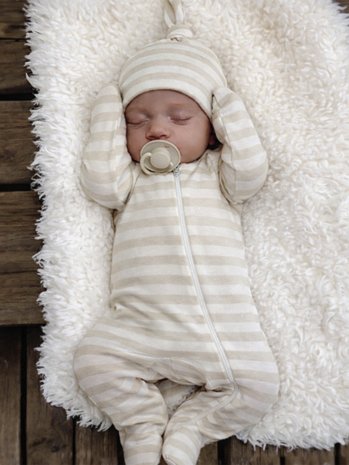 Sleeping baby in a striped outfit and hat, nestled on a fluffy white blanket.
