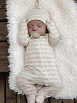 Sleeping baby in a striped outfit and hat, nestled on a fluffy white blanket.