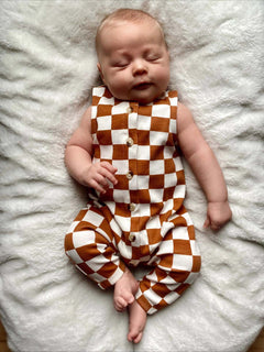 Baby sleeping on a soft blanket, wearing a brown and white checkered outfit, with a peaceful expression.